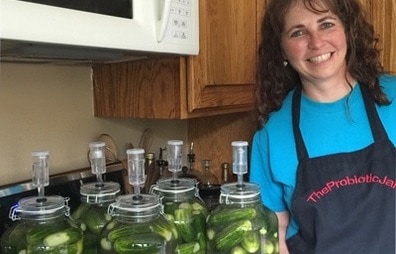 Kelly Caraway standing next to five liter Probiotic Jars of Fermented Dill Pickles.