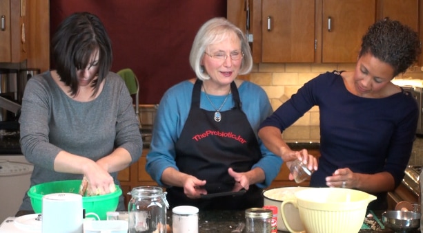 Linda Cox teaching her sauerkraut class with two helpers measuring salt and slicing cabbage on a mandolin.